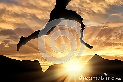 Disabled athlete with prosthetic leg jumping across rock on sunset Stock Photo