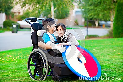 Disabled brother hugging older sister in wheelchair outdoors Stock Photo