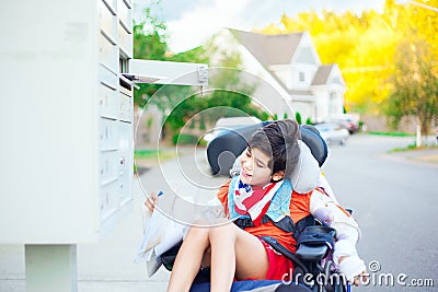 Disabled little boy in wheelchair getting mail from mailbox Stock Photo