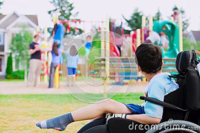 Disabled little boy in wheelchair watching children play on play Stock Photo