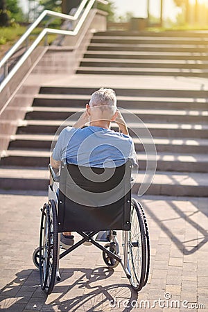 A man in a wheel chair sitting backside near the stairs outdoors Stock Photo