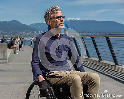 Disabled man in wheelchair.Thoughtful concentrated handicapped man touching wheels sitting in profile while moving ahead Editorial Stock Photo