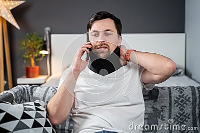 Disabled painful man with neck brace talking on phone at home. Man with spine trauma in neck brace cervical call Stock Photo