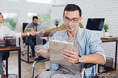 Disabled person in the wheelchair works in the office. In his hands is a tablet. Stock Photo