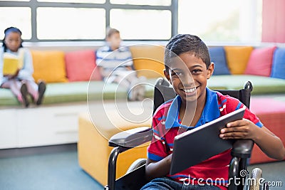 Disabled schoolboy on wheelchair using digital tablet in library Stock Photo