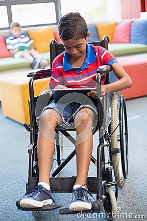 Disabled schoolboy on wheelchair using digital tablet in library Stock Photo