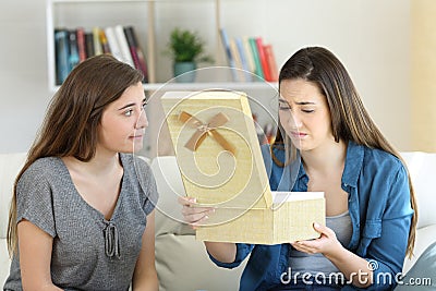 Disappointed girl opening a gift beside her friend Stock Photo
