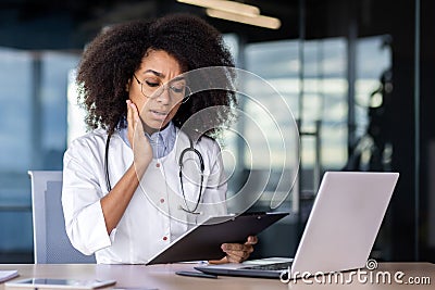 Disappointed hispanic woman therapist looking at clipboard with papers and feeling worried. Caring female nurse in Stock Photo