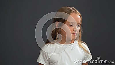 Disappointment little girl with long blond hair, looking thoughtful down wearing white t-shirt and black pants isolated Stock Photo