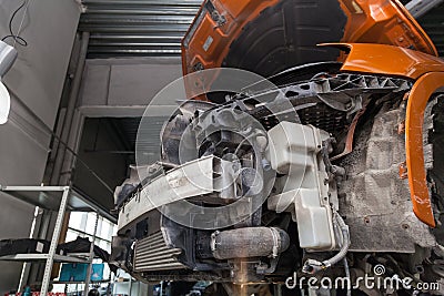 Disassembled orange car in the workshop raised on the lift prepared for repair: front end, hood and bumper removed, internal Stock Photo