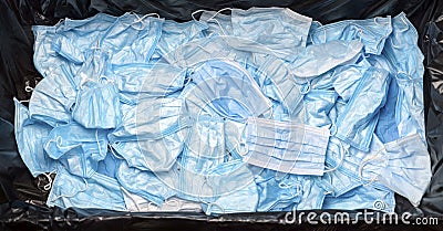 Discarded medical waste mask on virus banner in garbage can. Contaminated used trash disposable masks disposal after Covid-19 Stock Photo