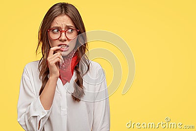 Discontent puzzled girl looks anxiously with worried expression aside, keeps fore finger near mouth, afraids of Stock Photo