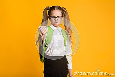 Discontented Schoolgirl Gesturing Thumbs Down Over Yellow Background Stock Photo