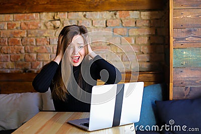 Disgruntled and shocked female person using laptop and sitting at cafe. Stock Photo