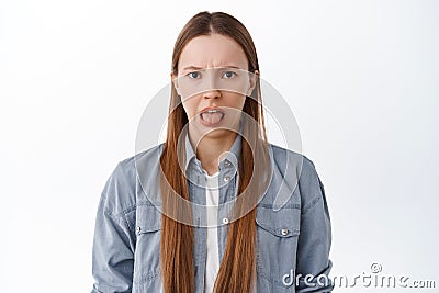 Disgusted teenage girl shows tongue and grimaces from bad taste, disgusting smell, something awful and stinky, standing Stock Photo