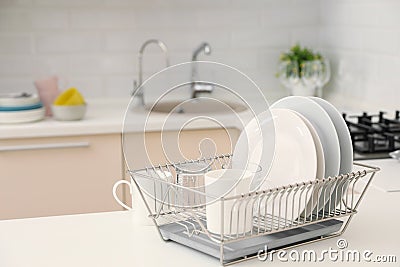 Dish drainer with clean dinnerware on table in kitchen Stock Photo