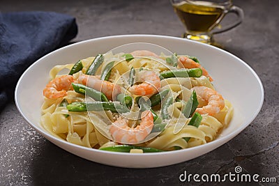 Dish of Tagliatelle with shrimps and green beans with grated Parmesan cheese on dark stone table. Pasta seafood. Mediterranean Stock Photo