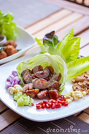 A dish of Thai style fermented sausage with side herbs, chili, lime, ginger, cashew nut. garlic and shallot on dining table. Stock Photo