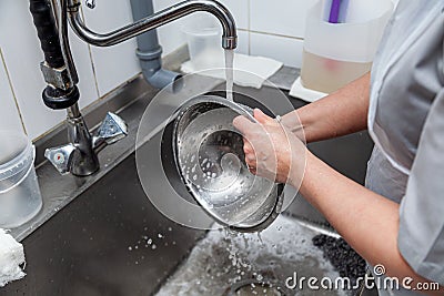 Dishwasher in uniform washes griddle with foam and sponge under the tap water Stock Photo