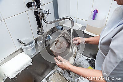 Dishwasher in uniform washes griddle with foam and sponge under the tap water Stock Photo