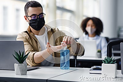 Disinfection and social distancing in office during COVID-19 epidemic. Young man worker in protective mask cleans his Stock Photo