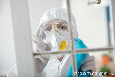 Woman in white workwear and respirator disinfecting the window Stock Photo