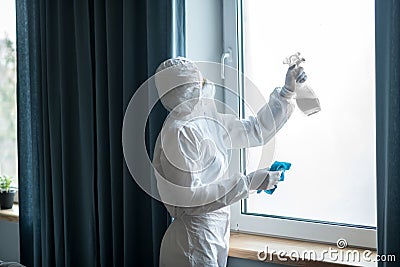 Woman in white workwear and respirator doing disinfection at home Stock Photo