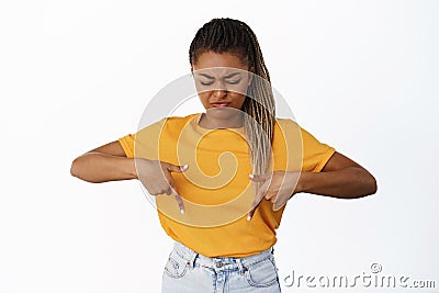 Dislike. Reluctant young Black woman pointing and looking down with skeptical, displeased face expression, grimacing Stock Photo