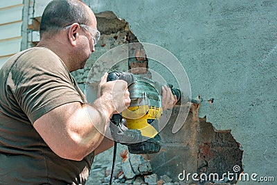 Dismantling walls and openings with an electric jackhammer. The worker in goggles performs repair work Stock Photo