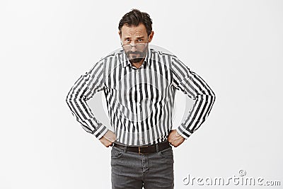 Disobedience will be punished. Serious-looking strict grandfather in glasses and striped shirt, holding hands on waist Stock Photo
