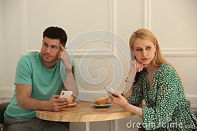 Displeased man and woman with smartphones in cafe. Failed first date Stock Photo