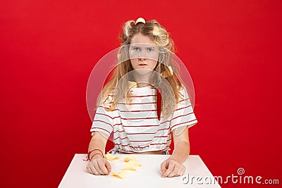 Displeased, sad, offended blonde teenage girl with orange citrus peels and chili pepper in hair and clothes sit at table Stock Photo