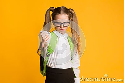 Displeased Schoolgirl Gesturing Thumbs Down In Dislike Posing In Studio Stock Photo