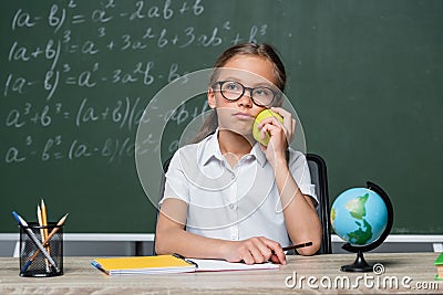 displeased schoolgirl holding apple near globe Stock Photo