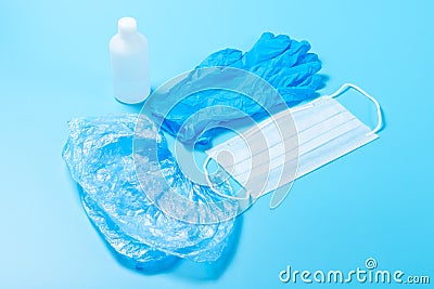 A disposable medical mask,one white bottle of antiseptic, a blue latex glove and Shoe covers on a blue background. The concept of Stock Photo