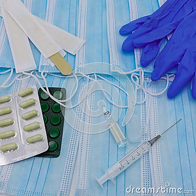 Disposable medical masks are spread out. On top of them lie latex gloves, wooden spatulas, packs of pills Stock Photo