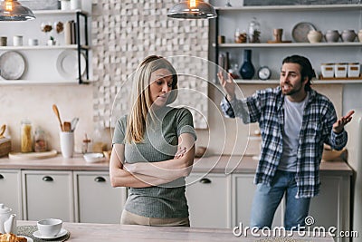 Dissatisfied angry caucasian millennial man with stubble spreads his arms to sides swears at sad blonde woman Stock Photo