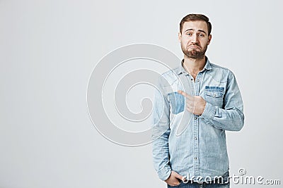 Dissatisfied guy with stubble sees something unpleasant, indicates with forefinger at copy space for promotional text Stock Photo