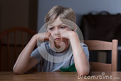 Dissatisfied kid sitting at table Stock Photo