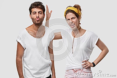 Dissatisfied spouse keeps hand on waist, raises hand and dissatisfied with husbands behaviour who flirts with other Stock Photo