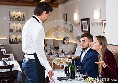 Dissatisfied young couple talking to apologetic waiter Stock Photo