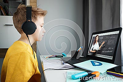 Distance learning, a boy in headphones sits at a table at home looking in a beech laptop. The concept of online education, home Stock Photo