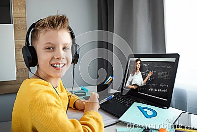 Distance learning, a boy in headphones sits at a table at home looking in a beech laptop. The concept of online education, home Stock Photo