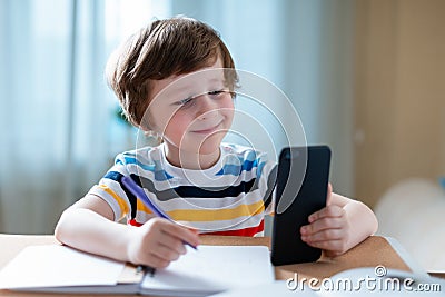 Distance learning online education. Caucasian smile kid boy studying at home with smartphone and doing school homework Stock Photo