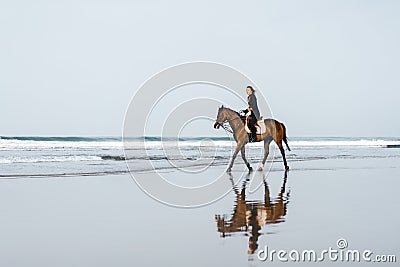 distant view of woman riding horse on sandy beach Stock Photo