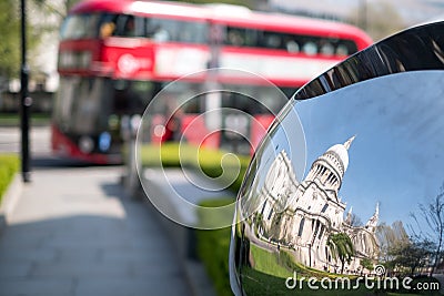 Distorted reflection of St Paul`s Cathedral, reflected in surface of mirror sculpture. Blurred red London bus in background. Editorial Stock Photo