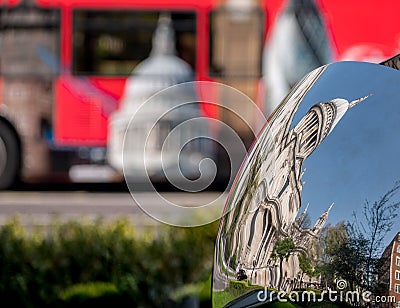 Distorted reflection of St Paul`s Cathedral, reflected in surface of mirror sculpture. Blurred red London bus in background. Editorial Stock Photo