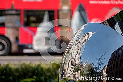 Distorted reflection of St Paul`s Cathedral, reflected in surface of mirror sculpture. Blurred red London bus in background. Editorial Stock Photo