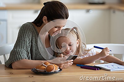 Distracted from drawing little preschool girl peeking into mother s smartphone. Stock Photo