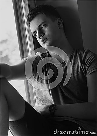 Distressed teenager boy sitting on window Stock Photo